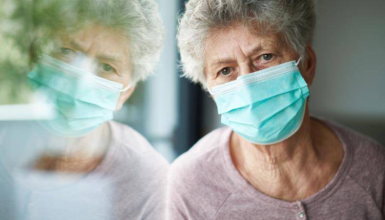 Older female with mask leaning against window