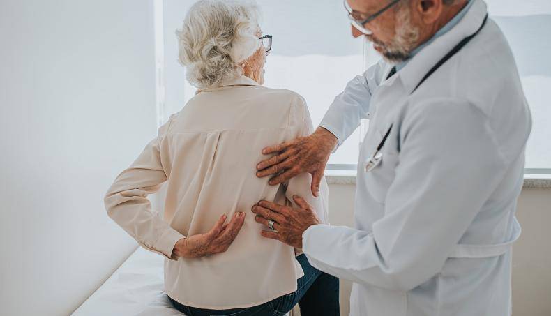 Physician examining senior patient lower back for bone and joint decline.