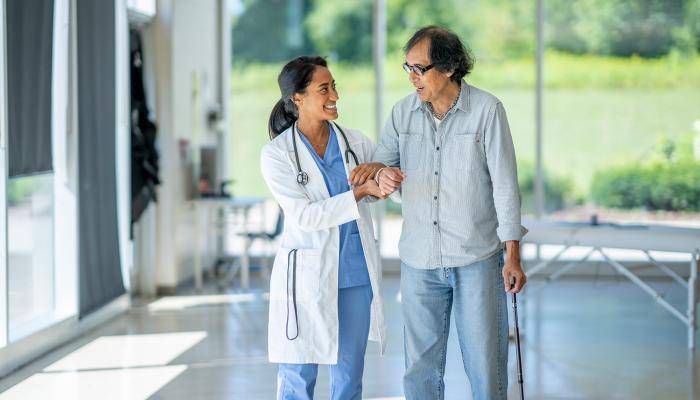 A physician walking alongside a senior arms intwined as they discuss treatment.